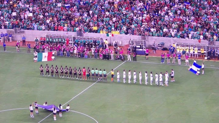 National teams lined up before a Gold Cup match as fans fill the stadium stands.